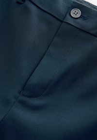 Merensininen housukangas, jossa on sileä pinta, yksinkertainen nappisuljenta ja hillitty taskudetalji.