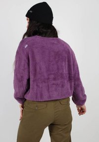 Pull en laine violet, ample, à col rond et manches longues. Associé à un pantalon vert olive, affichant un style décontracté.