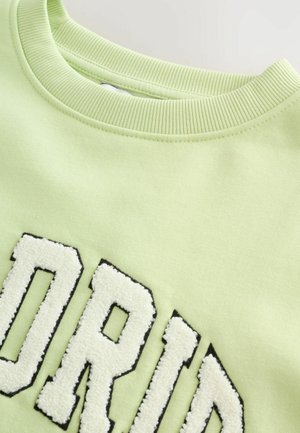 Lys grøn sweatshirt med ribbet hals. Forsiden har blød, hvid frotté-tekst med sort outline. Blødt stof.
