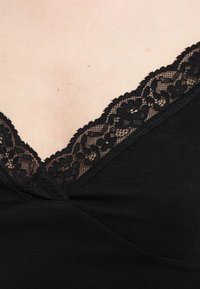 Μαύρο ένδυμα με φλοράλ δαντέλα κατά μήκος του ντεκολτέ, που δείχνει ανοιχτόχρωμο δέρμα με μερικά μικρά κόκκινα σημάδια.