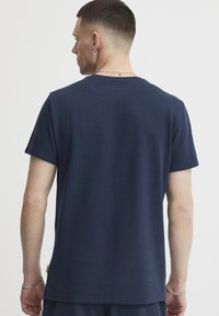Tricou din bumbac de culoare albastru marin, cu guler rotund, mâneci scurte și un finisaj texturat. Are o tivă dreaptă și un detaliu de branding minim.