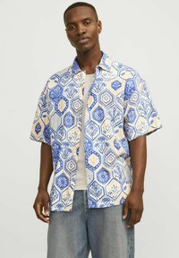 Korte mouwen shirt met een blauw, wit en beige hexagonaal patroon, versierd met bloemontwerpen. De stof lijkt lichtgewicht en ademend te zijn.