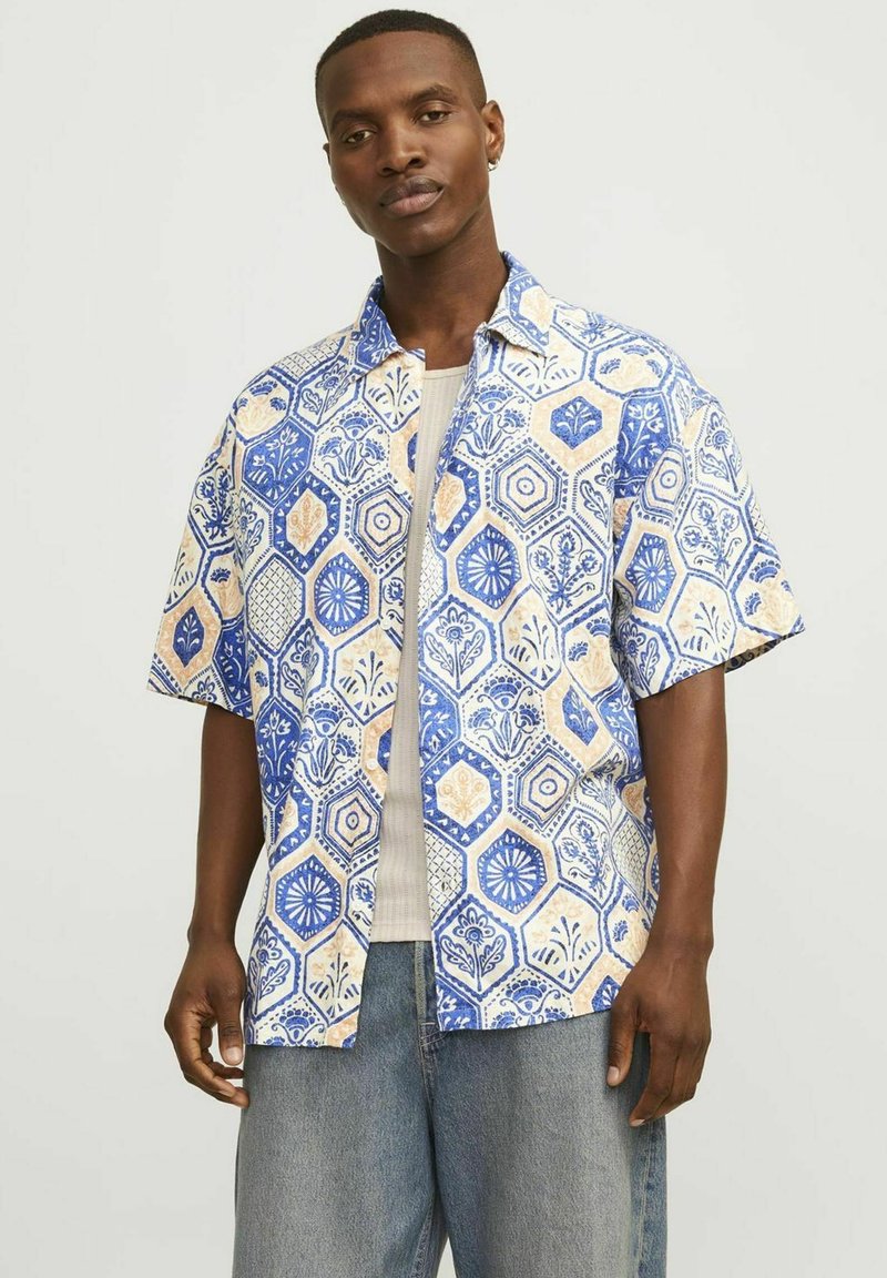 Korte mouwen shirt met een blauw, wit en beige hexagonaal patroon, versierd met bloemontwerpen. De stof lijkt lichtgewicht en ademend te zijn.