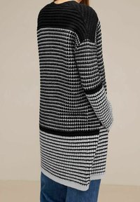 Pletený kardigan v černé a šedé barvě s žebrovaným vrškem a strukturovaným vzorem. Má dlouhý, volný střih a boční rozparky pro snadný pohyb.