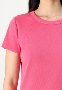 T-shirt ajusté à manches courtes en rose vif, fabriqué en tissu côtelé avec un col rond classique et une texture lisse.