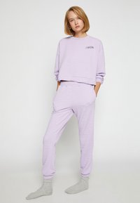 Conjunto de loungewear acolchado morado que incluye un sudadera corta y amplia con caja y pantalones con cordón y bolsillos laterales. La textura es suave y ligeramente elevada.