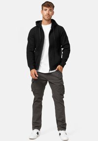Black zip-up hoodie with drawstrings and two front pockets, paired with gray cargo pants and white sneakers with black accents.