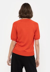 Skrócony sweter z krótkimi rękawami w jasnym pomarańczowym kolorze z prążkowanym dekoltem i dołem. Miękka tekstura, dopasowany krój i rękawy raglanowe.