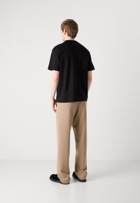 Czarny t-shirt z krótkim rękawem w połączeniu z beżowymi spodniami o szerokich nogawkach i czarnymi butami, widok z tyłu na neutralnym tle.