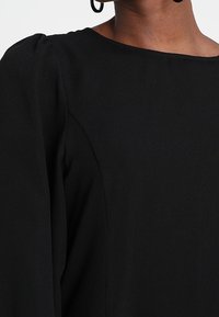 Schwarzes Kleidungsstück aus einem glatten, leicht strukturierten Stoff mit rundem Ausschnitt und puffärmeligen Details. Einfaches und elegantes Design.