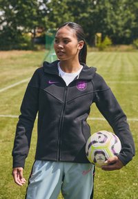 Melnā cepure ar rāvējslēdzēju, kurai ir kapuce, ar purpura Nike logo un Anglijas emblēmu. Gaiši pelēki šorti ar rozā akcentiem. Tur rokās daudzkrāsains futbola bumba.