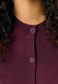 Cardigan en maille bourgogne avec un col rond et deux boutons assortis. Texture côtelée le long des bords et de la patte de boutonnage.