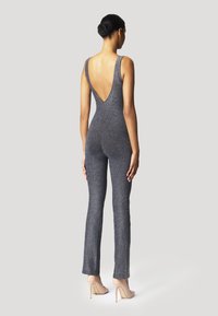 Combinaison sans manches gris foncé, avec un dos en V profond, un design ajusté, des jambes évasées, et une texture légèrement scintillante. Talons hauts beiges portés.