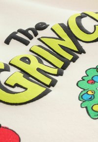 Biely textil s výraznými čiernymi a neónovo žltými písmenami, ktoré píšu "Grinch." Obsahuje farebný zelený karikatúrny vianočný stromček s ozdobami.