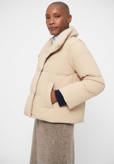 Beige puffer jacket with a high collar, quilted design, side pockets, and navy knit cuffs. Smooth texture, lightweight appearance.