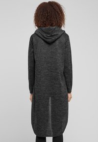 Lang, hette cardigan i mørkegrå teksturert stoff. Har lange ermer og en rund kant, som gir en avslappet passform.