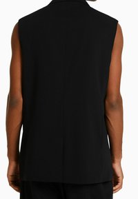 Svart ärmlös väst med en skarp krage och rena linjer, med en slät yta och minimalistisk design, visad från baksidan.