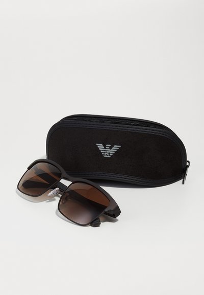 Black sunglasses with a matte finish, brown gradient lenses, and rubberized accents. Accompanied by a black protective case.