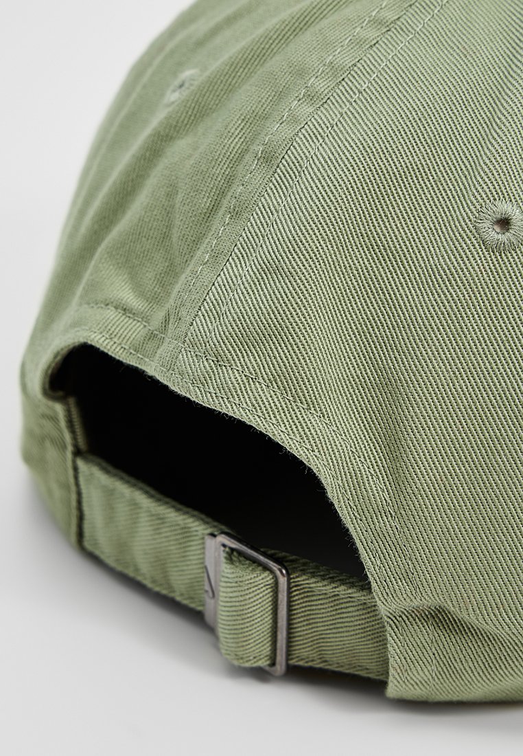 Gorra de béisbol de tela verde claro con la parte trasera ajustable y hebilla de metal sobre un fondo blanco liso.