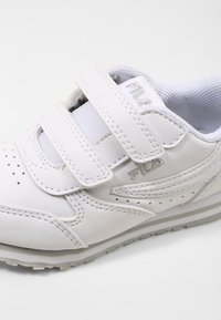 Sneaker bianco in pelle con fibbie in velcro, linguetta in mesh imbottita, punta perforata e suola in gomma grigia con dettagli del logo sottili.