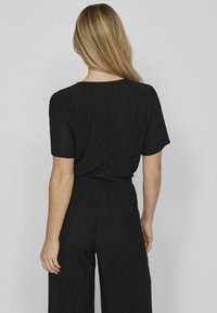 Zwarte geribbelde jumpsuit met korte mouwen, ruime pasvorm en wijde pijpen. Toont een gestructureerd oppervlak en heeft een elastische taille voor comfort.