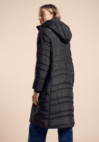 Zwarte puffy jas met horizontale quiltpatronen, een capuchon en manchetboorden, met een ronde logo patch op de linker mouw en een knielange ontwerp.