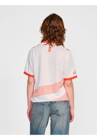 Witte sporttrui met oranje accenten, met een gestructureerd geometrisch patroon aan de onderkant. Bevat het "OCSC" logo op de achterkant.