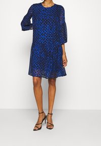 Blå leopardmönstrad klänning med rund halsringning, trekvartslånga genomskinliga ärmar och en flödande silhuett. Buren med svarta remsandaler.