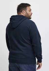 Felpa blu navy in cotone, dotata di tasca a marsupio, polsini e orlo a coste, cappuccio con coulisse e texture morbida.