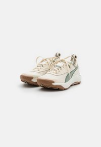 Sneaker leggere in crema con accenti verdi, materiali in rete e sintetico, suole texturizzate e occhielli rinforzati per i lacci.