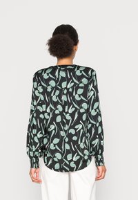 Blusa nera con un motivo a foglia verde, tessuto leggero, maniche lunghe e una vestibilità rilassata con orlo arrotondato e dettaglio plissettato sul dorso.