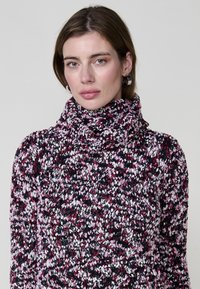 Pull à col roulé tricoté en fil multicolore avec des nuances de rose, noir et blanc ; tissu texturé avec un design épais.