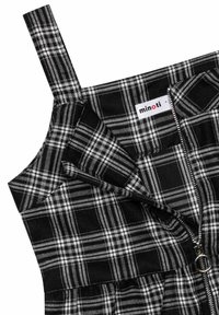 Robe écossaise noir et blanc avec des bretelles larges et une fermeture éclair à l'avant, présentant une tirette en métal circulaire, avec l'étiquette de la marque Minoti à l'intérieur.