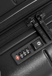 Black hard-shell suitcase close-up featuring dual zippers, a combination lock, and a red accent in the lock design. Smooth texture.