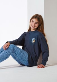 Long-sleeve navy shirt with text design on the chest, paired with light blue leggings featuring a dark abstract pattern.