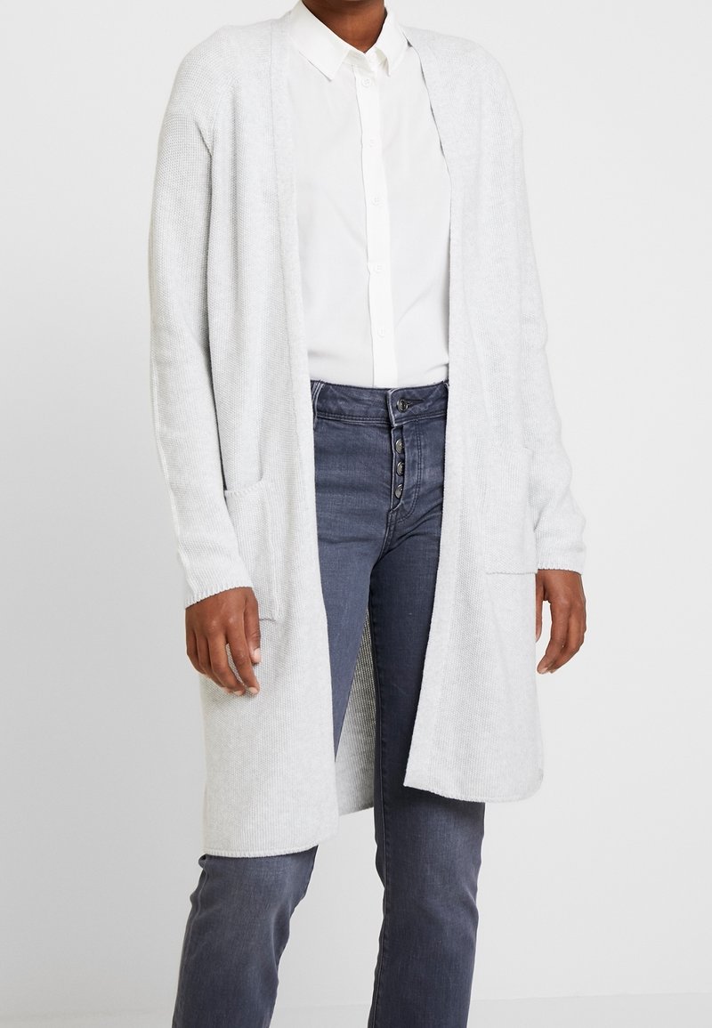 Cardigan gris clair en maille douce, avec un devant ouvert, des poignets côtelés, deux poches avant et une coupe décontractée.