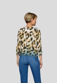 Leopardenmuster-Pullover mit rundem Ausschnitt, Dreiviertelärmeln und geripptem Saum in Creme-, Grün- und Brauntönen. Kombiniert mit blauen Jeans.