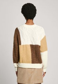 Pull en maille blanc, marron et beige avec un motif torsadé. Coupe carrée, poignets et ourlet côtelés. Tissu doux et texturé.