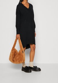 Abito nero a maglia con scollatura a V e maniche lunghe, abbinato a una borsa fluffy beige e scarpe nere stringate sopra calze beige.