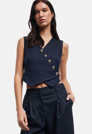 Gilet à rayures navy avec un col en V, accents de boutons dorés et une coupe courte, associé à un pantalon à rayures taille haute.