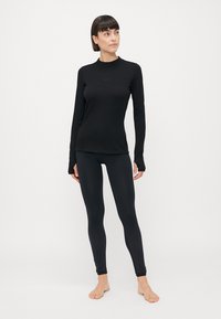 Svart langermet topp og leggings laget av glatt, elastisk stoff. Toppen har rund hals og subtil merkevare; leggings har et teksturert mønster.