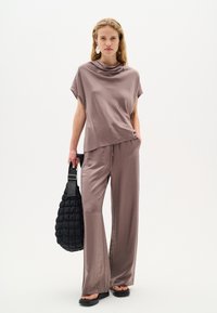 Top ampio di colore malva con colletto a bix, abbinato a pantaloni larghi coordinati. Presenta una borsa nera textured e sandali neri piatti.