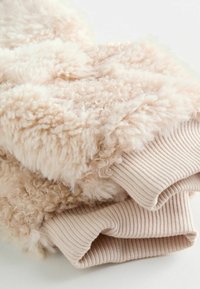 Puszysty, jasnobeżowy sweter o teksturowej, kręconej powierzchni i prążkowanych mankietach. Miękka, pluszowa tkanina; luźny krój.