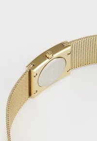 Gold mesh strap watch with a rectangular gold-tone case and a silver face. Features a CK logo and secure hardware on the strap.