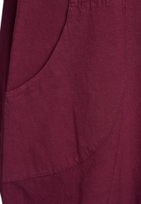 Burgundy klädbomull med en mjuk textur, med detaljer som rundade fickor och subtila sömnadsakcenter. Nära vy av designen.
