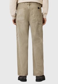 Beige cotton cargo pants with back pockets, straight cut, subtle texture, and waist branding detail. No visible fasteners or patterns.