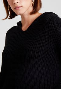 Maglione nero lavorato a maglia con design a V e tessuto testurizzato. La vista ravvicinata mette in evidenza il motivo intrecciato e la vestibilità rilassata.