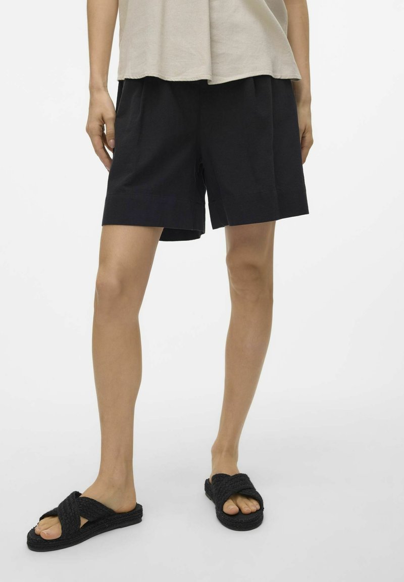 Shorts neri di cotone con una vestibilità comoda e orlo ripiegato, abbinati a sandali neri con intreccio. Sfondo bianco semplice.