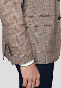 Brązowa marynarka w kratę z fakturowanej tkaniny, z niebieskimi liniami, pojedynczą kieszenią na piersi i czterema guzikami na rękawie.