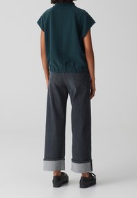 Maglione turchese a maniche corte con elastico in vita, abbinato a jeans grigi a gamba larga con orli risvoltati e scarpe nere stringate.